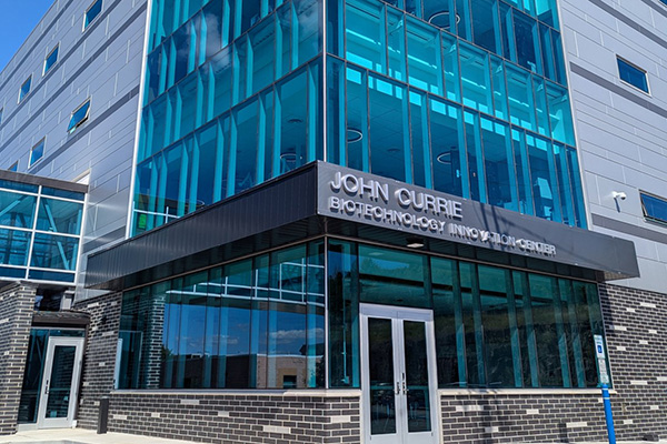 View of building exterior with birck and glass; sign reads John Currie Biotechnology Innovation Center