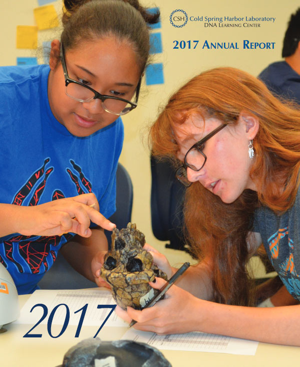 Annual report cover with a photo of two female high school students examining a recreation of an ancient hominid skull in a DNALC lab classroom