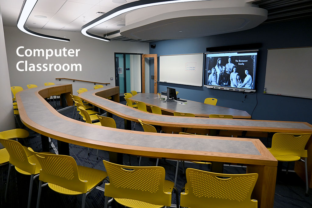 Classroom with curved desks and yellow chair focusing on large smartboard monitor