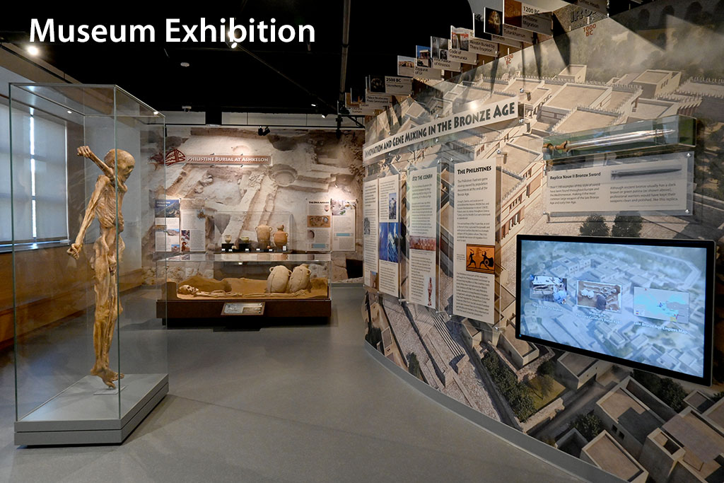 View of museum exhibition with a mummy sculpture in a glass case, a replica burial sculpture, and museum labeling mounted on walls will large mural backdrops