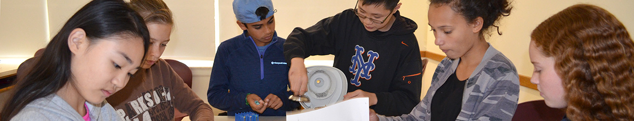 six students at a DNALC laboratory bench reviewing papers or loading a centrifuge during an experiment.