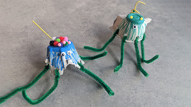 Two critters with egg carton body, moving eyes, pipe cleaner legs, colorful pom pom hair, and curly/staight tails.
