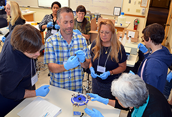 Several educators wearing blue surgical gloves in metabarcoding research teacher training gathered around a centrifuge
